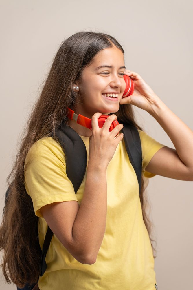 A happy young student laughs while putting on red headphones to listen to music.