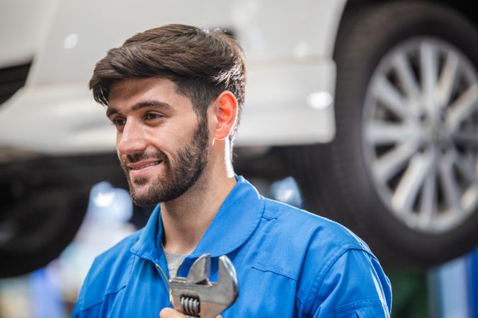 Smiling male mechanic with a beard holding wrench at auto garage