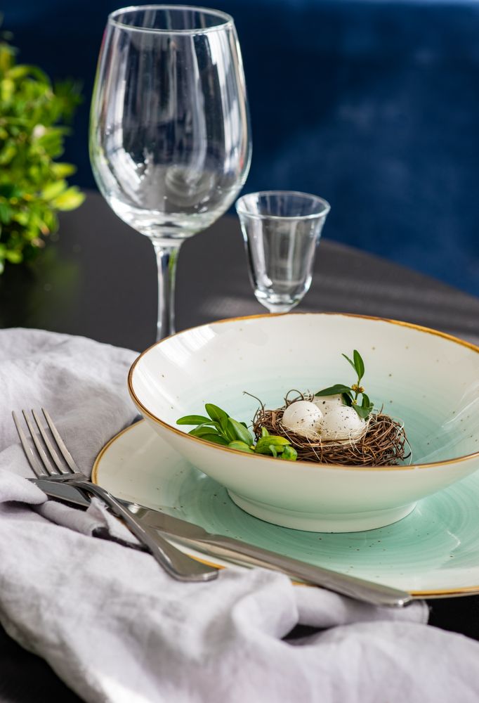 Easter table setting with bird's nest decor in ceramic bowl next to glassware