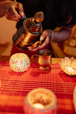 Cropped image of woman pouring tea in a copper mug beside Diwali's lit ornament