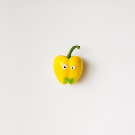 Yellow pepper with googly eyes and bowtie pasta on light background