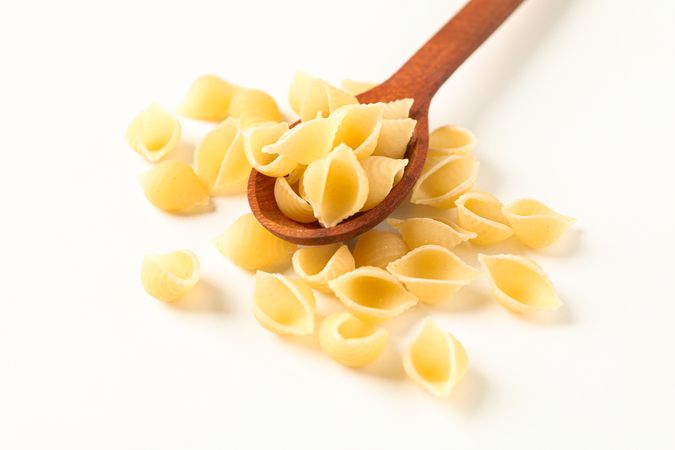 Wooden spoon with pasta on plain background, space for text. Dry uncooked whole pasta