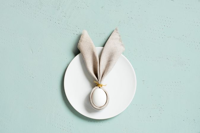 Bunny ear shaped napkin on plate on blue background with copy space