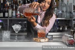 Bartender pouring stirred Negroni cocktail into an old-fashion glass with ice cubes 4BEdW5