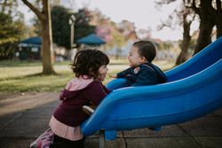 Young girl greets her toddler brother at the bottom of a slide
