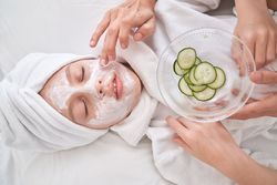 Unrecognizable woman putting cream mask with cucumber slices on