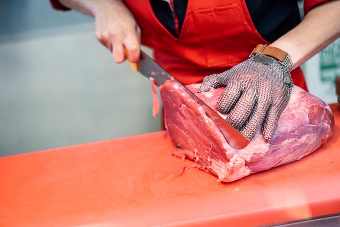 Close up of butcher in apron cutting raw meat