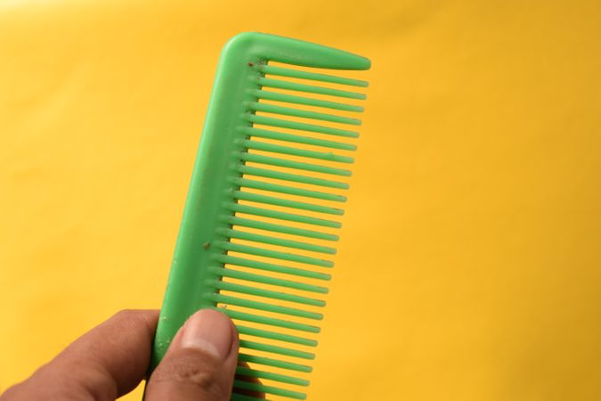 Hand holding bright green hair comb against yellow background