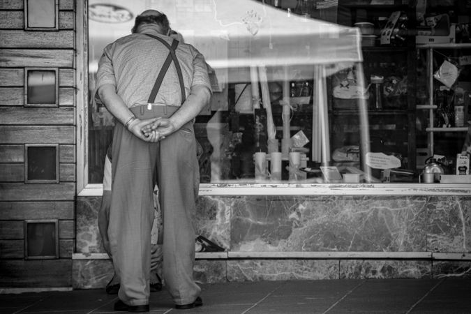 Back view of an older man looking at shop window in grayscale