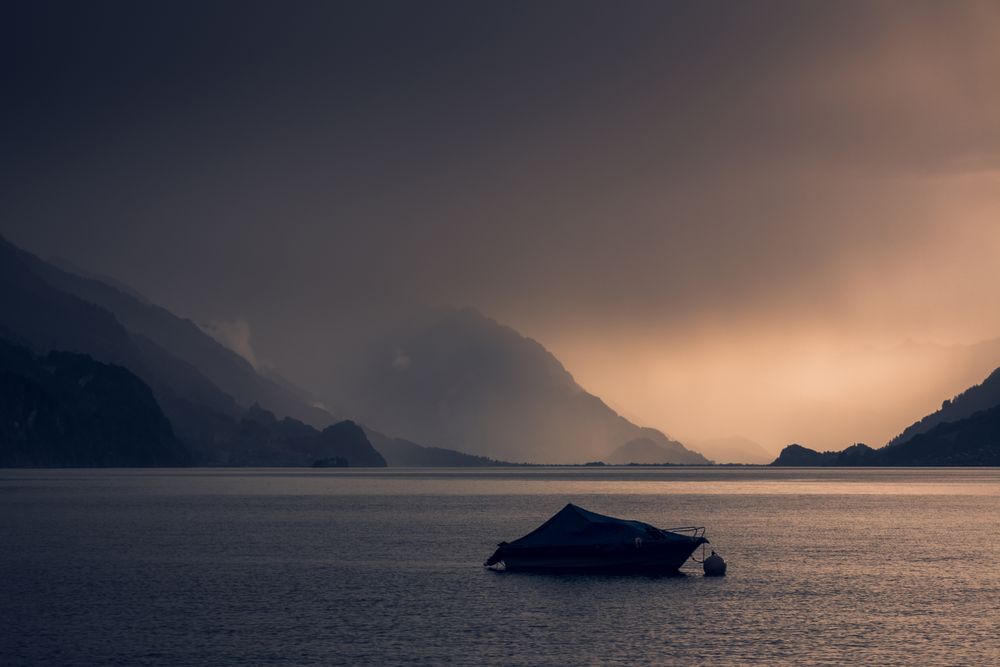 Lonely yacht in gray water with dark mountains under cloudy sky