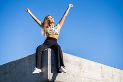 Happy woman sitting on corner of roof with arms up