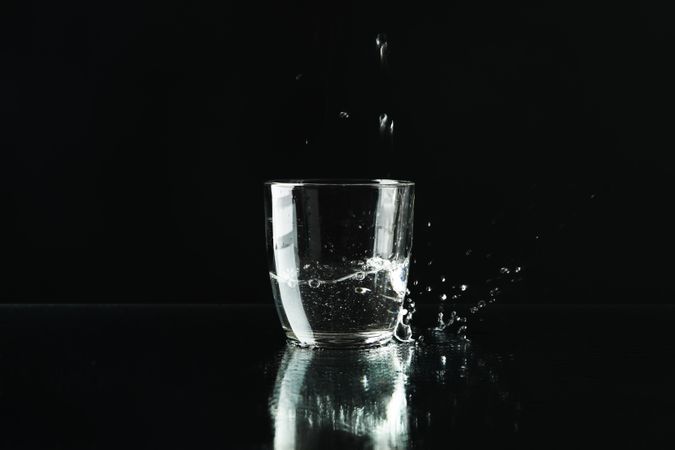 Drops of water falling into glass in dark room