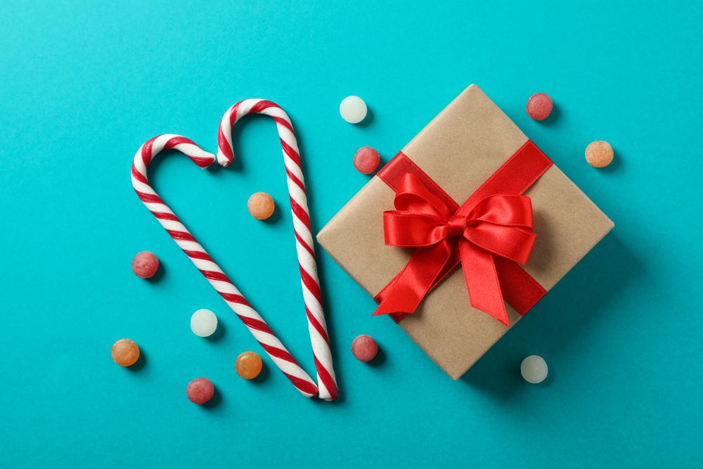 Sweet candy canes and gift box on turquoise background, space for text
