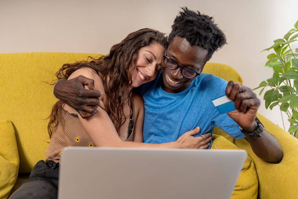 An affectionate diverse couple hugging happily after making a successful online purchase with a credit card.