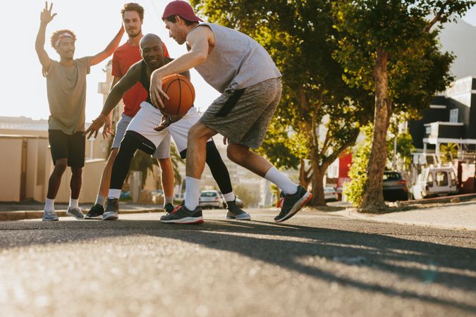 Men playing basketball game on a sunny day on an empty street
