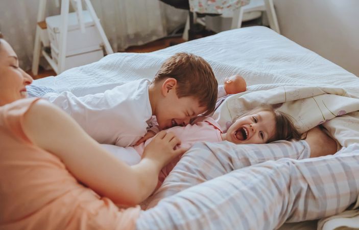 Closeup of happy boy and little girl playing in bed on a relaxed morning with mother looking on