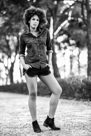 Monochrome full body shot of female standing outside in denim shirt looking away from camera