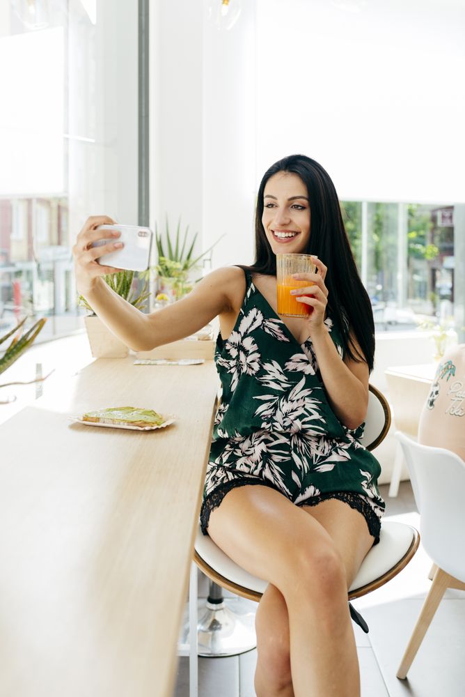 Woman with healthy drink taking selfie in cafe