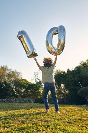 Unrecognizable boy with number balloons during birthday on meado
