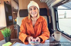 Woman in orange shirt sitting and smiling in van with smartphone 0VkD35