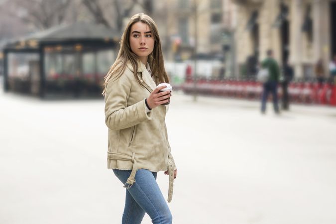 Portrait of woman walking in a city street, with a to go coffee in hands