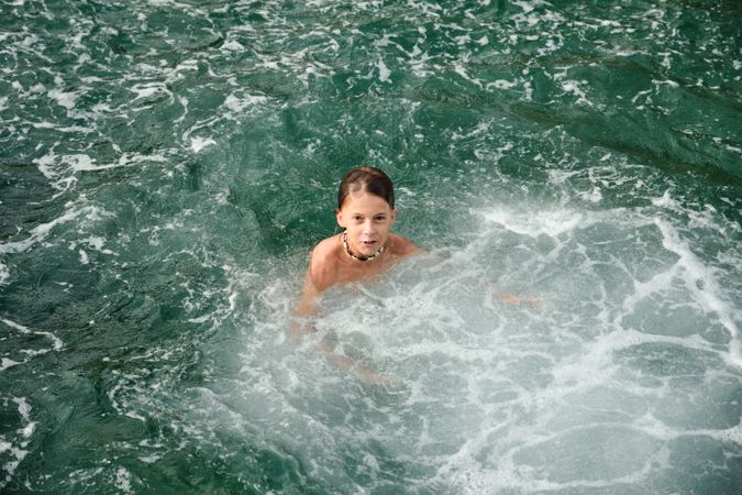 Shirtless boy in the sea looking at the camera and relaxing