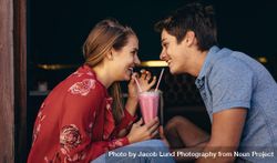 Couple on a date and enjoying a milkshake with two straws looking at each other 5rl7pb