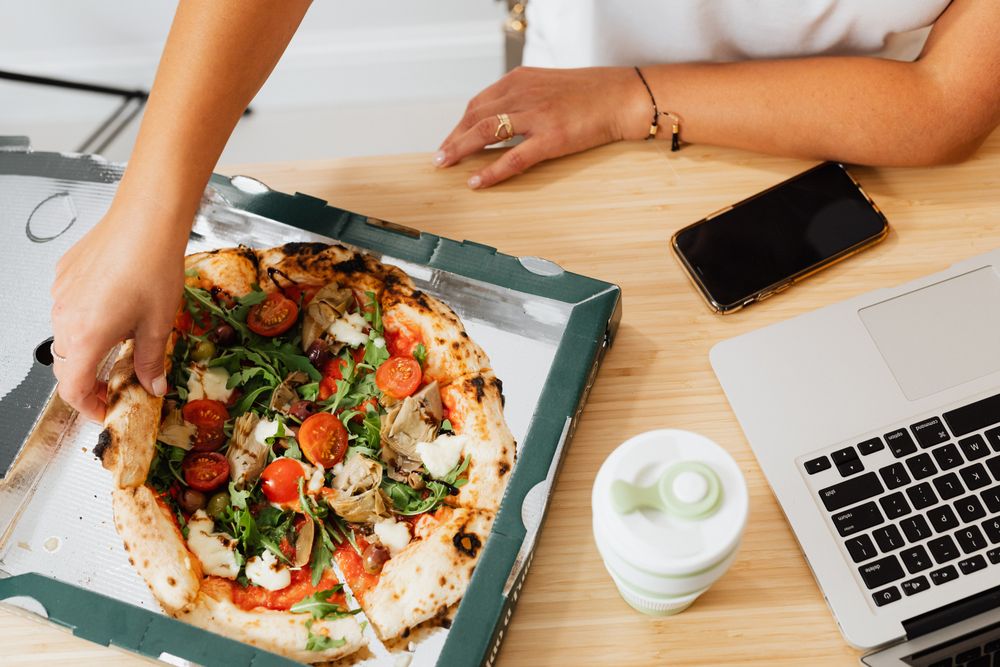 Cropped image of woman eating pizza at work