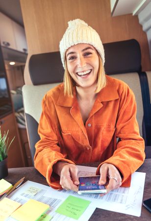 Woman in orange shirt sitting and laughing in van with smartphone, vertical