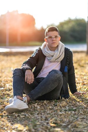 Teenage male in striking eyewear sitting on grass in a city park