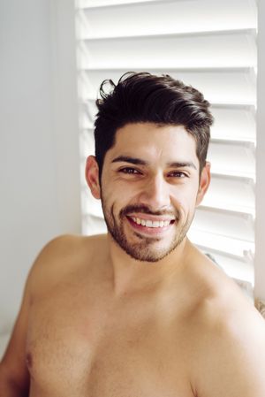 Young cheerful naked man leaning on window