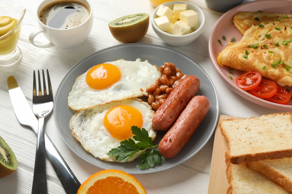 Two fried eggs sunny side up on plate with bacon and sausage on light wooden table