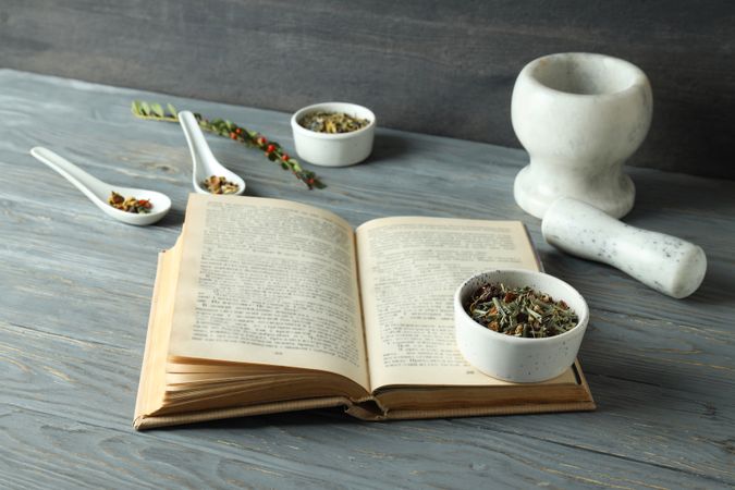 Book and herbs in bowls on wooden background