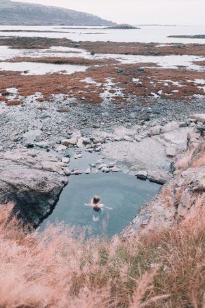 Woman in pond near hill on shore