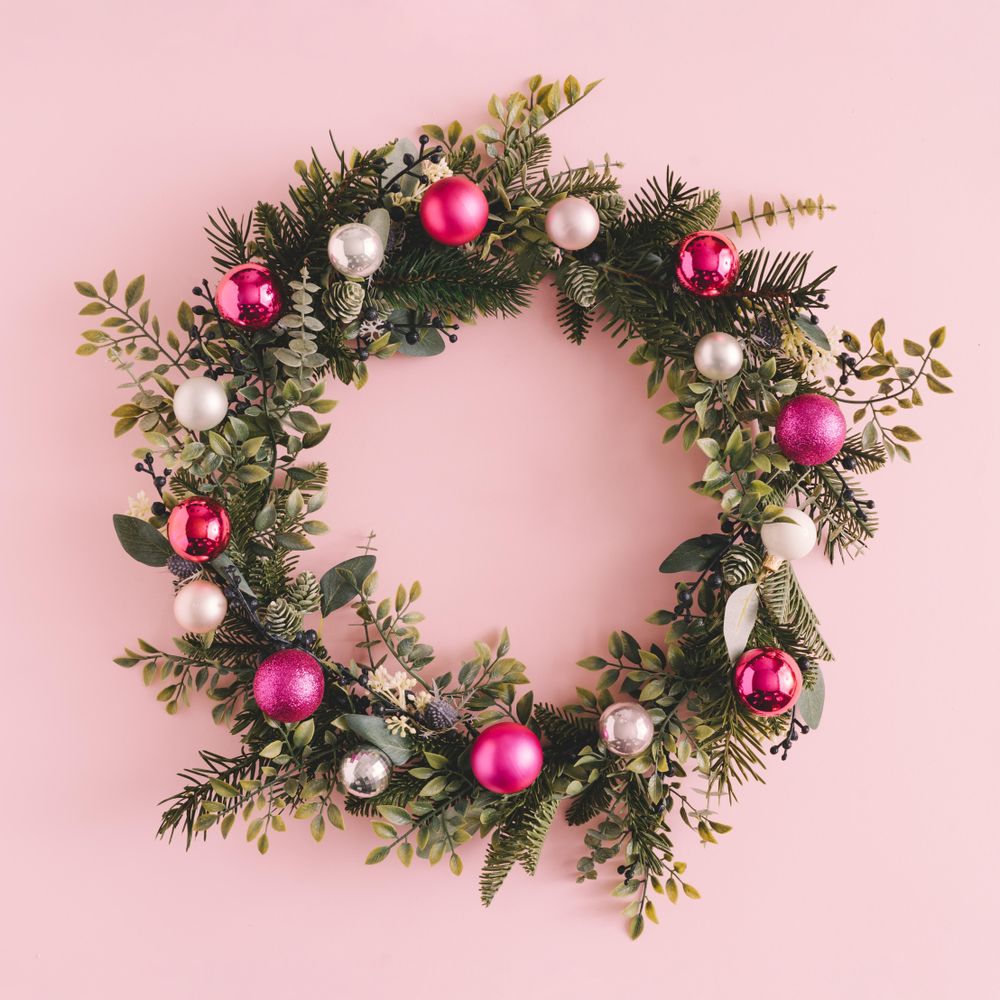 Christmas wreath made of decorative baubles and branches on pink background