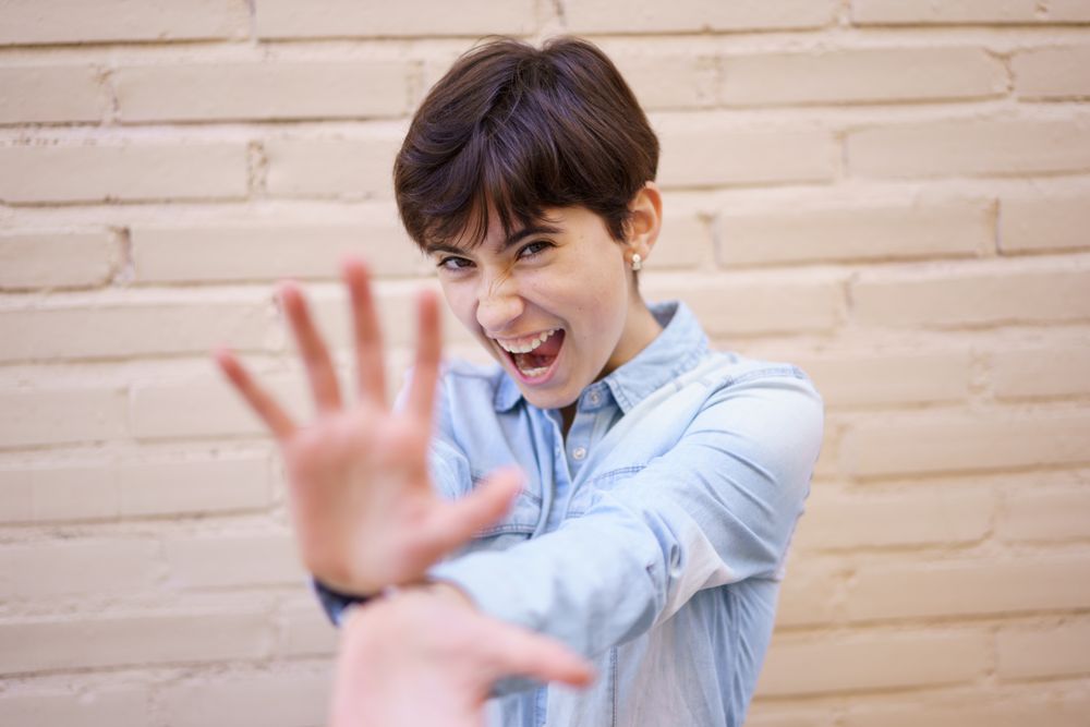 A Joyful and Cheerful Young Woman Playfully Posing Against a Colorful Brick Wall