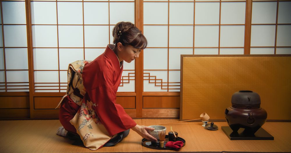 Asian Woman in Traditional Red Kimono with FLower Ornaments Trying the Tea From a Bowl