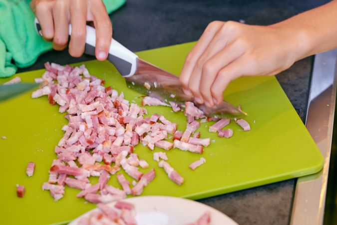 Crop person cutting smoked bacon while cooking in kitchen