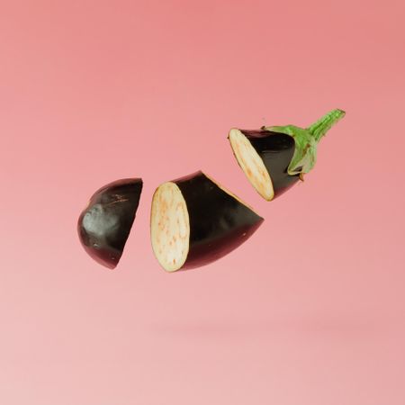 Sliced eggplant suspended on pastel pink background with copy space