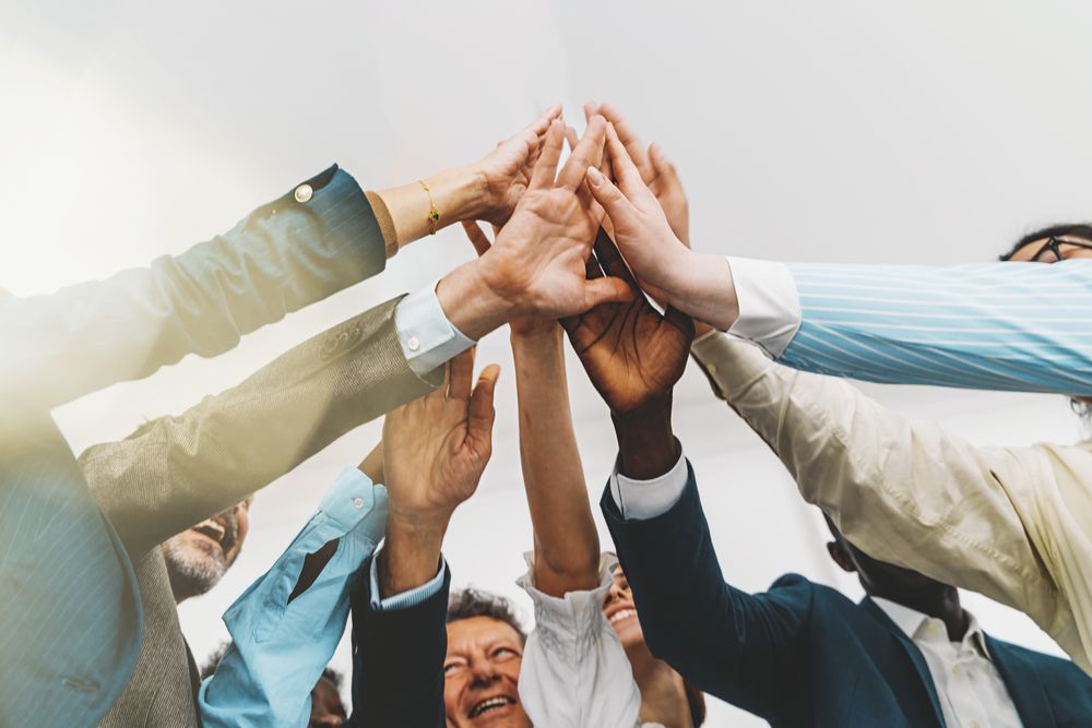 Low-angle shot of a diverse team of colleagues standing together in a bright office, giving a group high five