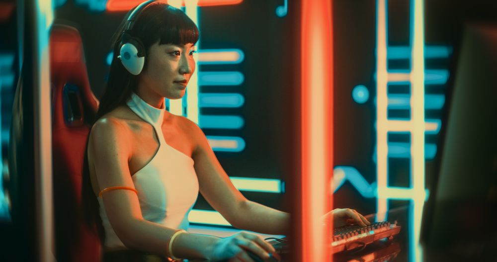Young Woman Wearing Futuristic Clothes and Neon Rings, Playing Video Games on a Desktop Computer.