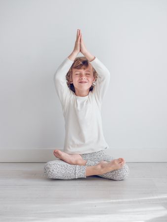 Boy in white pajamas leaning against the white wall of his house.