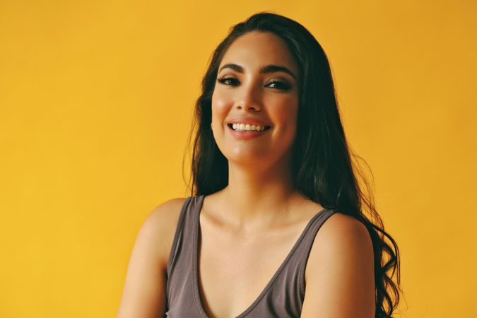 Smiling happy Hispanic woman looking at camera in yellow room, copy space