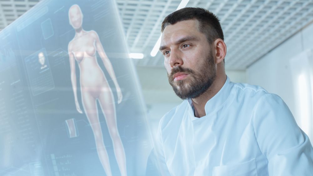 In the Futuristic Laboratory Male Scientist Works on His Transparent Computer Display with Graphic Projection of Human Body, Future Medicine Concept.