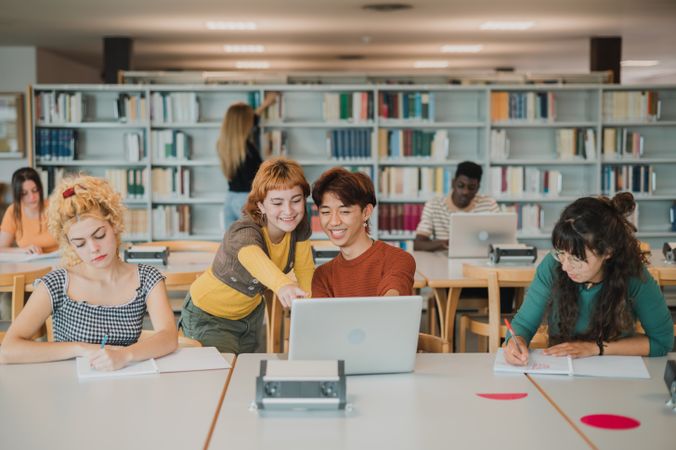 Multiethnic male and female students taking notes and using laptops in library