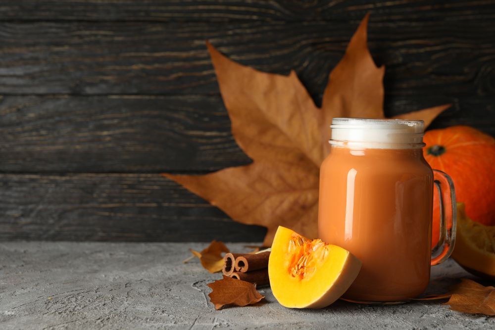Composition with pumpkin latte, pumpkin, leaves and cinnamon on gray table