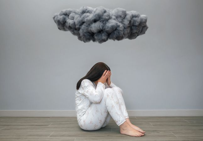 Woman covering her face with hands under a dark storm cloud