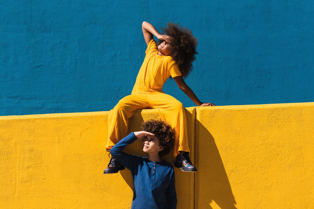 Black curly haired girl and boy resting near colorful wall