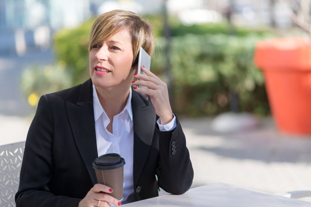 Woman sitting on table outside with coffee speaking on cell phone