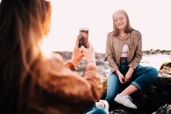 A young woman sitting outside has her photo taken by a friend